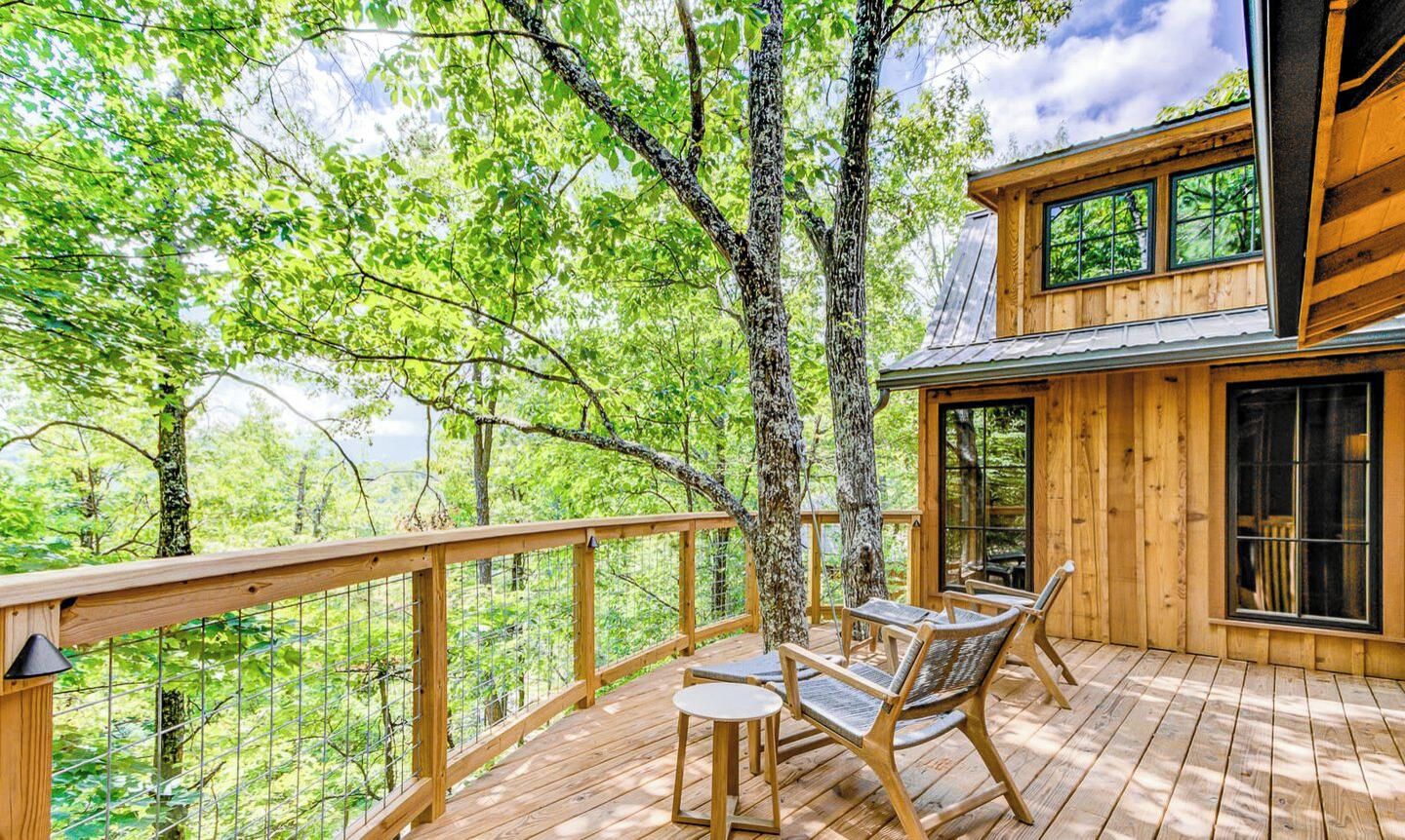 Une terrasse en bois avec une table et des chaises, entourée d’arbres.