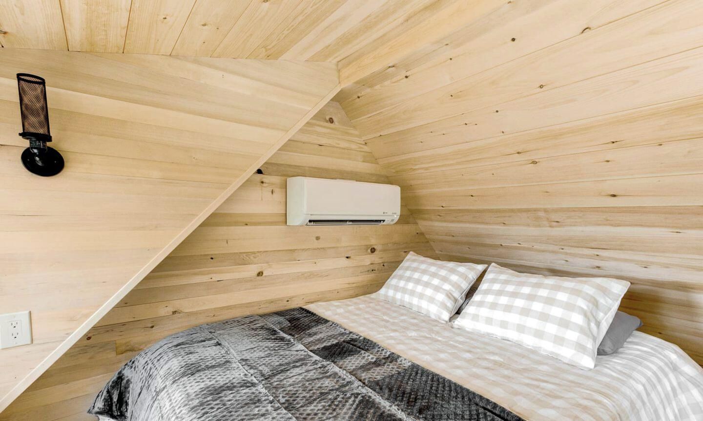 A room with a bed, a wall-mounted air conditioner, and a power outlet.