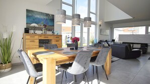 Uma sala de jantar moderna com mesa de madeira, cadeiras cinzas e luminárias pendentes.