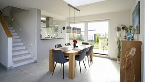 Uma sala de jantar moderna com mesa e cadeiras de madeira, uma escada e vista para o exterior.