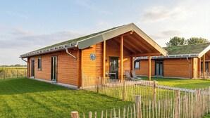 Eine Holzhütte mit überdachter Veranda, einem eingezäunten Hof und einem Rasen.