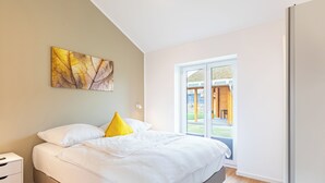 Ein Schlafzimmer mit Bett, Nachttisch, Fenster mit Blick ins Freie und einem an der Wand hängenden abstrakten Kunstwerk.