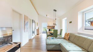 Ein modernes Wohnzimmer mit einem Ecksofa, einem Fernseher und einem Essbereich mit Stühlen und einem Tisch.