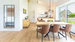 Et moderne køkken med hvide skabe, en træbordplade og udsigt til et grønt landskab gennem store vinduer.