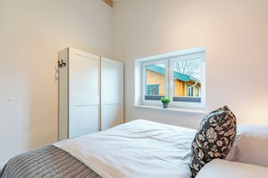 Ein Schlafzimmer mit Bett, Fenster, Kleiderschrank und Blick auf ein Gebäude.