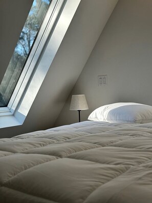 Een slaapkamer met een schuine kap, een raam, een lamp en een bed.