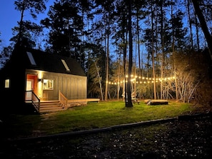 A cabin with a porch, a picnic table, and string lights in a forested area.