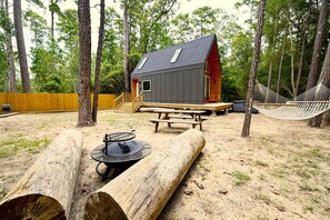Een blokhut met een terras, een hangmat, een picknicktafel en een vuurkuil, gelegen in een bebost gebied.