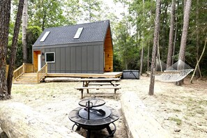 Eine Hütte mit Terrasse, Picknicktisch, Hängematte und Grill.