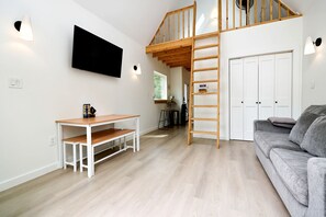 Una sala de estar moderna con un altillo de madera, un televisor de pantalla plana, una mesa de madera y un sofá gris.