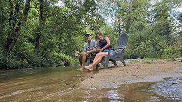 Two people sitting on a chair by a river in a forested area.