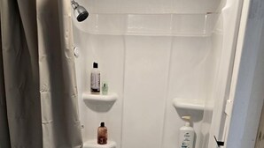 A shower with a beige curtain, a handheld showerhead, and shelves with toiletries. - Tranquil Creekside Tiny House in the Appalachian Mountains, Perfect for a Weekend to Disconnect (Purlear)