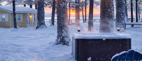Un espacio al aire libre cubierto de nieve con un jacuzzi, una chimenea y luces colgantes.