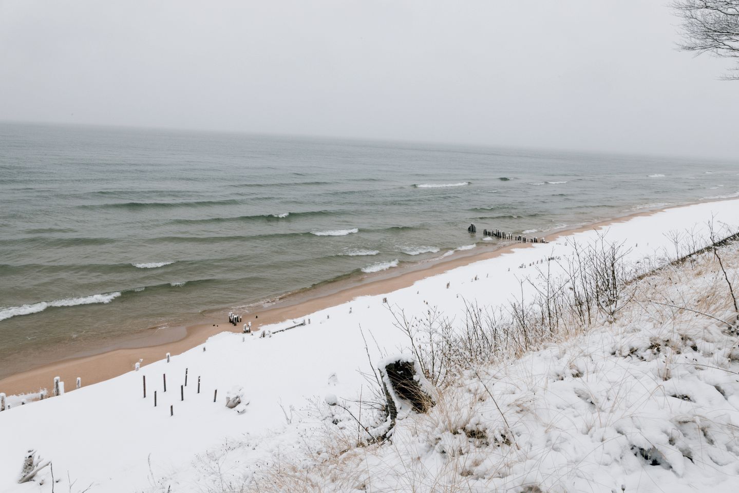 Une plage dont le sable est recouvert de neige et où se trouve une jetée en bois.