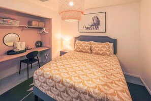 A bedroom with a bed, a desk, a chair, a lamp, and a framed picture on the wall.