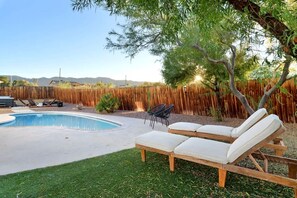A backyard with a swimming pool, lounge chairs, and a wooden fence.