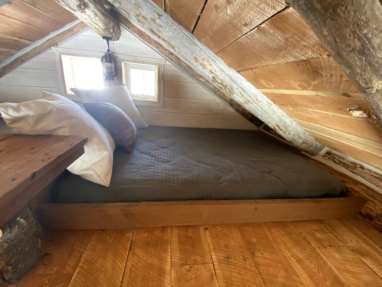 Une chambre aménagée en mezzanine avec un plancher en bois, un matelas, des oreillers et un luminaire suspendu.