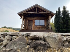 A wooden cabin with a stone foundation, large windows, and a wooden door.