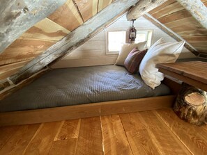 A loft bedroom with a wooden floor, a bed with a grey quilt, pillows, and a lantern.