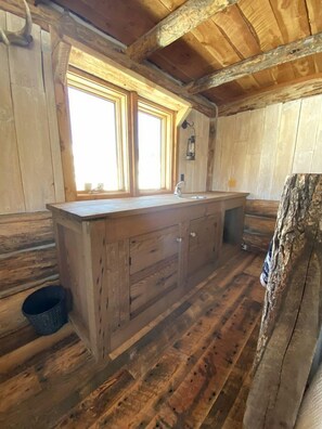 A rustic cabin interior with a wooden floor, a large window, and a sink.