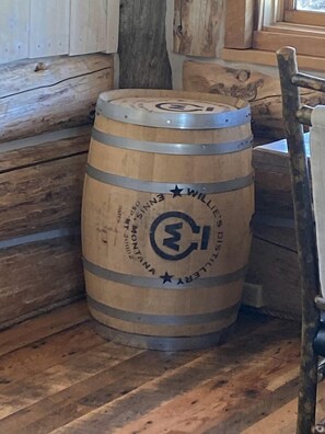 A wooden barrel with inscriptions and a logo, placed against a wooden wall with a window in the background.