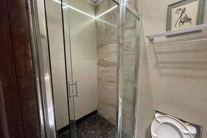 A bathroom with a glass shower enclosure, a toilet, and a marble wall. - BAYLIS HOTEL AND SUITES (Ikeja)