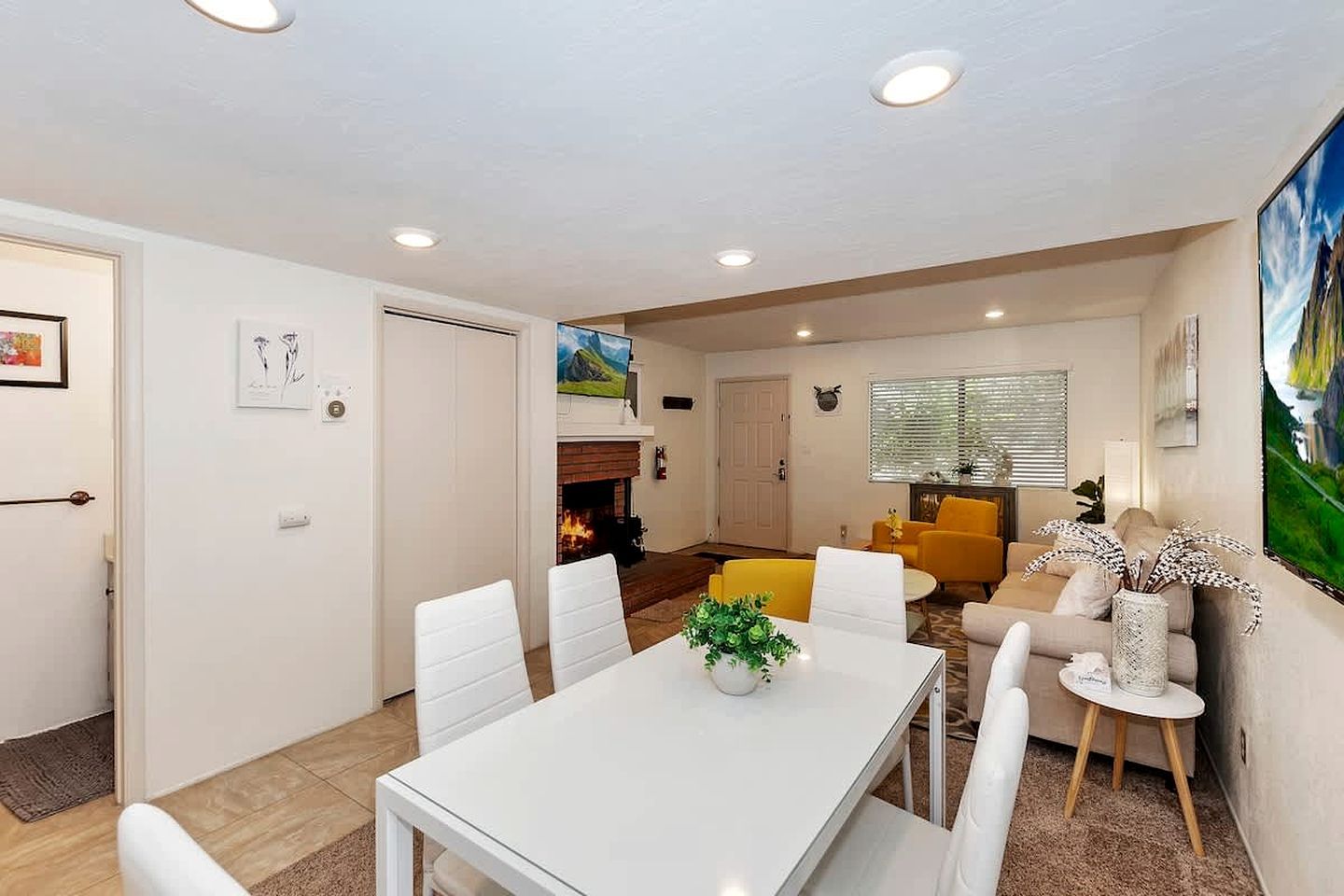 Un salon moderne avec une cheminée, un coin repas avec une table et des chaises blanches, et un fauteuil jaune.