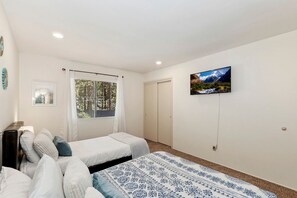 Ein Schlafzimmer mit zwei Betten, einem Fenster mit Jalousien, einem Bild an der Wand und einer Tür.