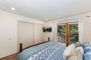 Ein Schlafzimmer mit einem Bett, einem Fernseher, einer Schiebetür zu einem Balkon und einer weißen Decke mit Einbaustrahlern.