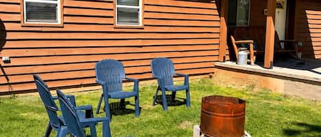 A wooden cabin with a green roof, outdoor seating with blue chairs, and a metal barrel.
