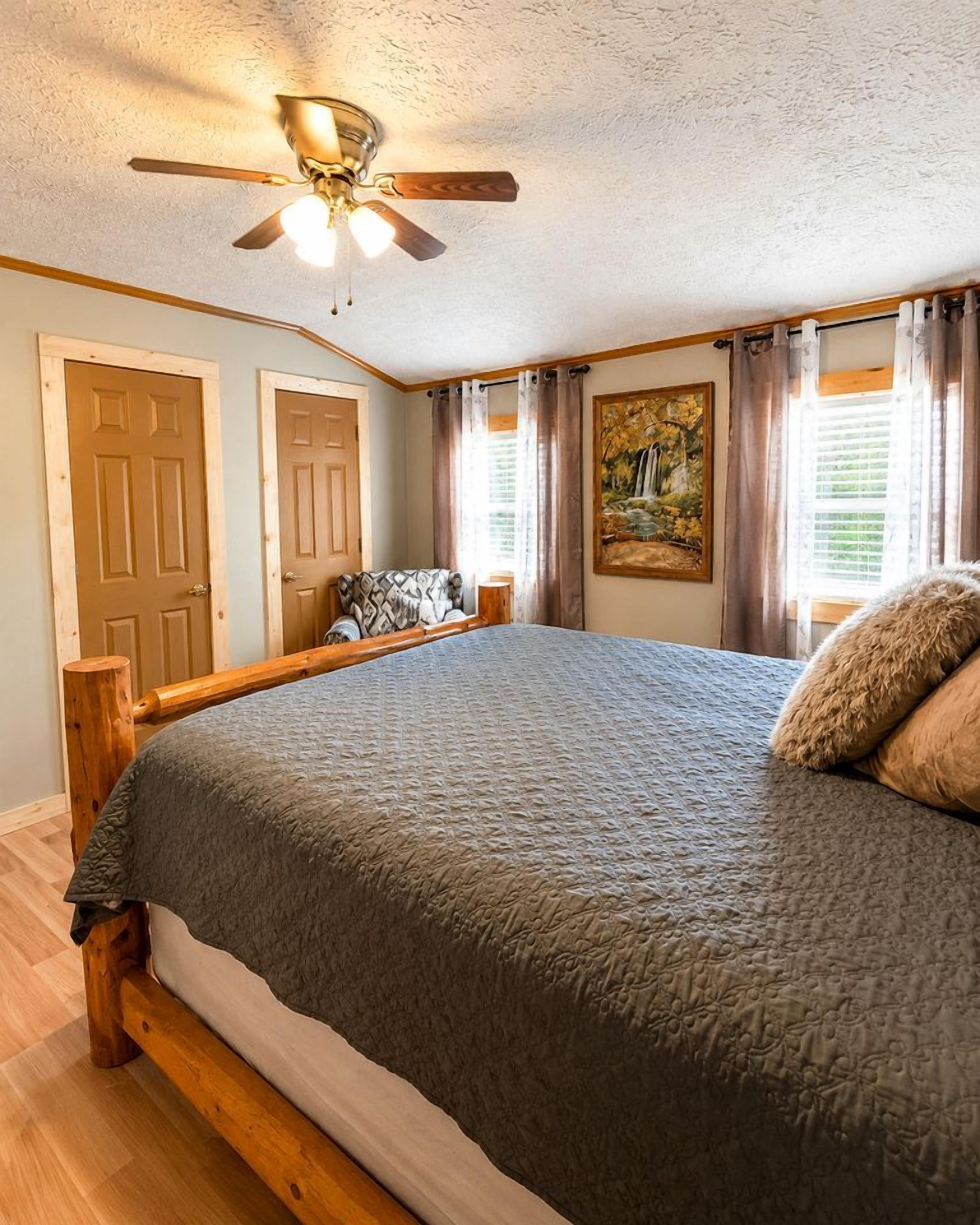A bedroom with a large bed, wooden headboard, a ceiling fan, and a painting on the wall.