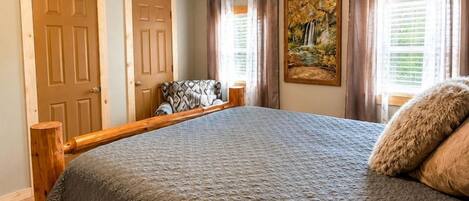 A bedroom with a large bed, wooden headboard, a ceiling fan, and a painting on the wall.