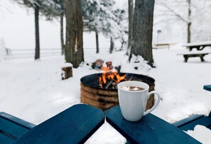 A snow-covered outdoor area with a fire pit and a white mug on a blue bench.