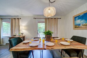 A dining area with a wooden table set for four, surrounded by chairs, with a hanging light fixture above. - Lovely Beach House Rental in Coastal Michigan, for Memorable Getaways to Muskegon (Muskegon)