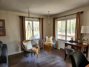 A room with two hanging chairs, a desk with a lamp, and a view of the outdoors. - Lovely Beach House Rental in Coastal Michigan, for Memorable Getaways to Muskegon (Muskegon)