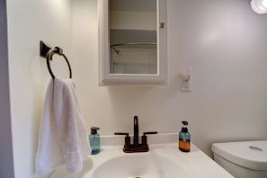 A bathroom with a white sink, a mirror, a towel rack, a toilet, and two soap dispensers. - Lovely Beach House Rental in Coastal Michigan, for Memorable Getaways to Muskegon (Muskegon)