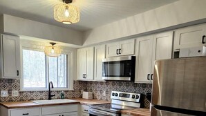 A modern kitchen with white cabinets, stainless steel appliances, and a patterned backsplash. - Lovely Beach House Rental in Coastal Michigan, for Memorable Getaways to Muskegon (Muskegon)