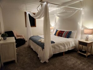 Une chambre à coucher avec un lit à baldaquin, des tables de chevet, une lampe et une petite table sur laquelle est posée une plante.