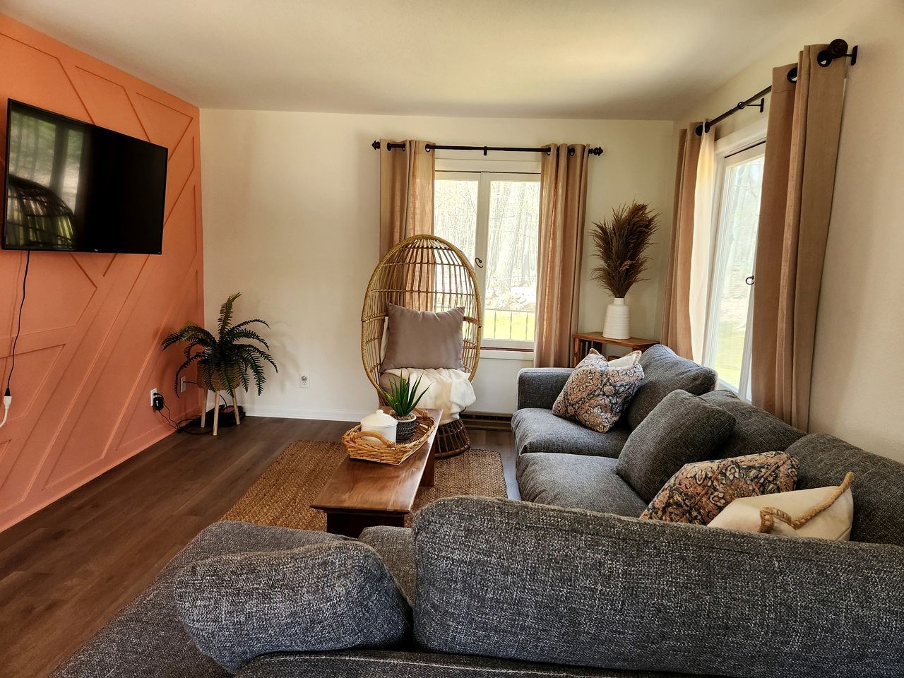 A living room with a sofa, a television, a window with curtains, and a plant.