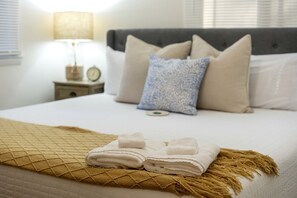A neatly made bed with a folded white towel, a patterned throw blanket, and a bedside table with a lamp and a clock. - Lovely Beach House Rental in Coastal Michigan, for Memorable Getaways to Muskegon (Muskegon)