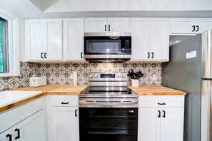 A kitchen with white cabinets, a microwave, a stove, and an oven. - Lovely Beach House Rental in Coastal Michigan, for Memorable Getaways to Muskegon (Muskegon)