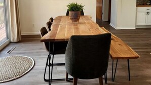 A modern dining area with a wooden table, black chairs, a hanging light fixture, and a potted plant. - Lovely Beach House Rental in Coastal Michigan, for Memorable Getaways to Muskegon (Muskegon)