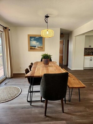 Un comedor moderno con una mesa de madera, sillas negras, una lámpara colgante y una planta en maceta.