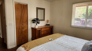 A bedroom with a bed, a wooden dresser, a mirror, and a window with blinds. - Lovely Beach House Rental in Coastal Michigan, for Memorable Getaways to Muskegon (Muskegon)