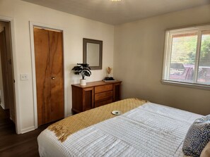 Ein Schlafzimmer mit einem Bett, einer Holzkommode, einem Spiegel und einem Fenster mit Jalousien.
