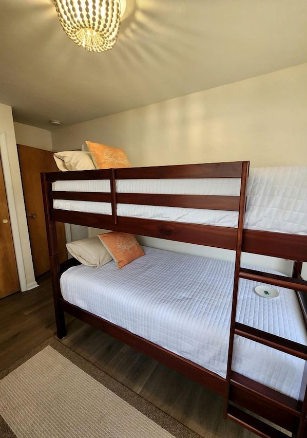 Una cama litera con estructura de madera, ropa de cama blanca y una mesita de noche pequeña.