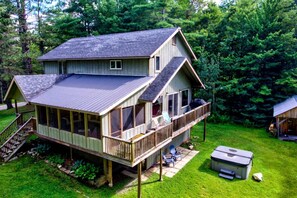 Eine zweistöckige Hütte mit einer Terrasse, einer Veranda und einem Whirlpool.