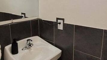 A bathroom with a pedestal sink, a mirror, a wall-mounted air conditioner, and a toilet paper holder.