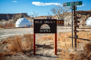 A sign for Blue Valley Domes with a desert landscape in the background.