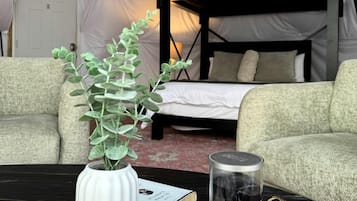 A bunk bed, a white vase with green leaves, and a candle on a tray in a tented room.